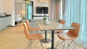 Quarto de hotel moderno com área de refeições, televisão na parede e uma grande janela com cortinas.