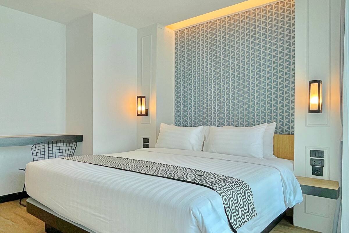 A modern hotel room with a large bed, two bedside tables, a patterned wall, and wall-mounted lights.