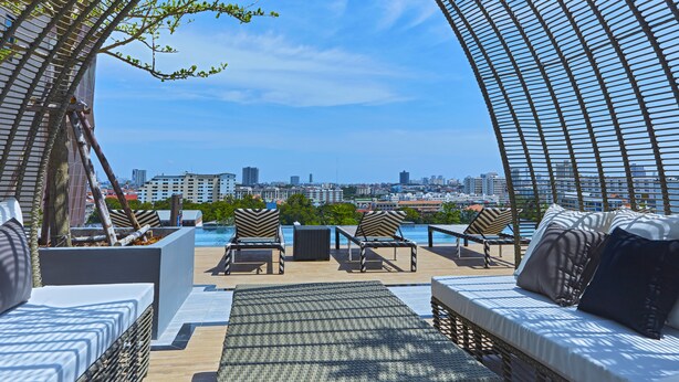 Um terraço com mobiliário de vime, piscina e vista para a cidade.