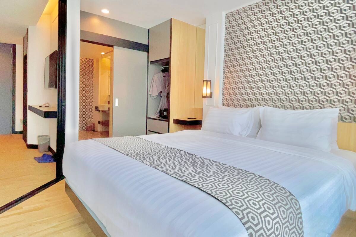 A hotel room with a large bed, a patterned headboard, and a bathroom visible through an open door.