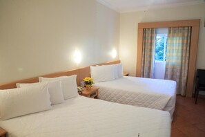 A hotel room with two beds, a nightstand with a telephone and a vase of flowers, and a window with curtains. - Itu Plaza Hotel (Itu)