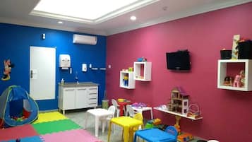 A children's playroom with colorful mats, play tables, chairs, and toys.