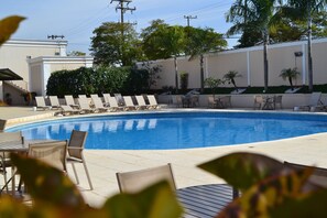 A swimming pool with lounge chairs and tables, surrounded by palm trees and a building in the background. - Itu Plaza Hotel (Itu)