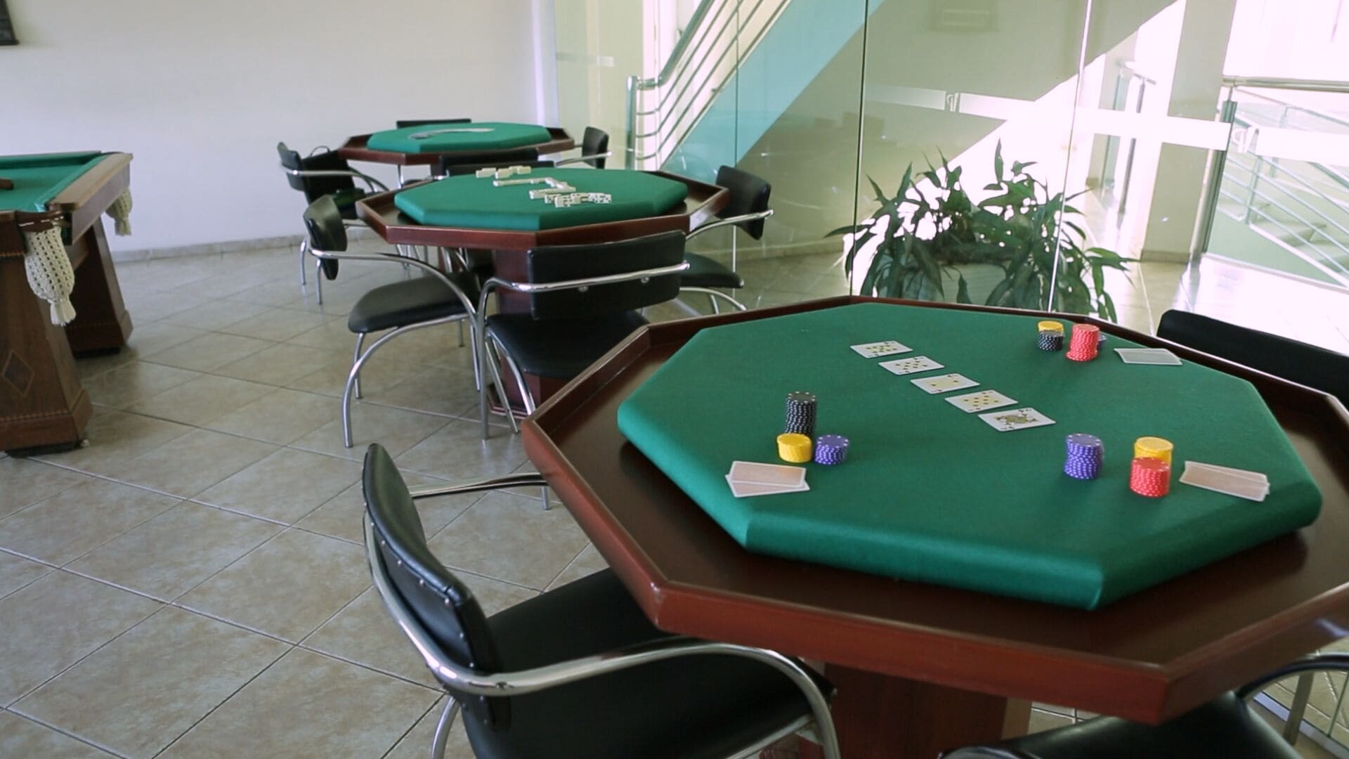 Una sala da casinò con diversi tavoli e sedie verdi, una scala e una pianta in vaso.