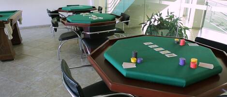 A casino room with multiple green tables and chairs, a staircase, and a potted plant.