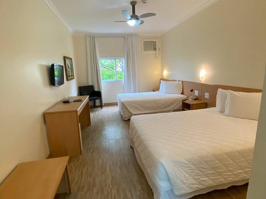 A hotel room with two beds, a desk, a chair, a ceiling fan, and a window with curtains.