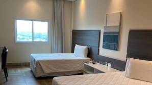 Habitación de hotel con dos camas, un escritorio, una silla y ventana con vistas.