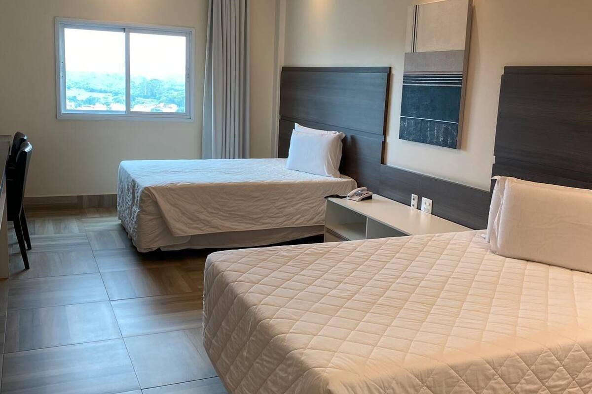 A hotel room with two beds, a desk, a chair, and a window with a view.