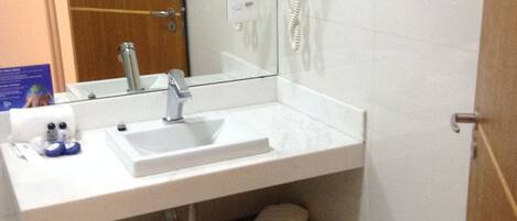 A bathroom with a white sink, a mirror, two hair dryers mounted on the wall, and a towel rack.