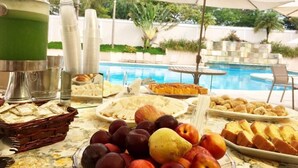 Una mesa de bufé con frutas, pasteles y un dispensador de bebidas junto a una piscina.