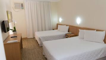 A hotel room with two beds, a desk, a telephone, and a wall-mounted air conditioner.