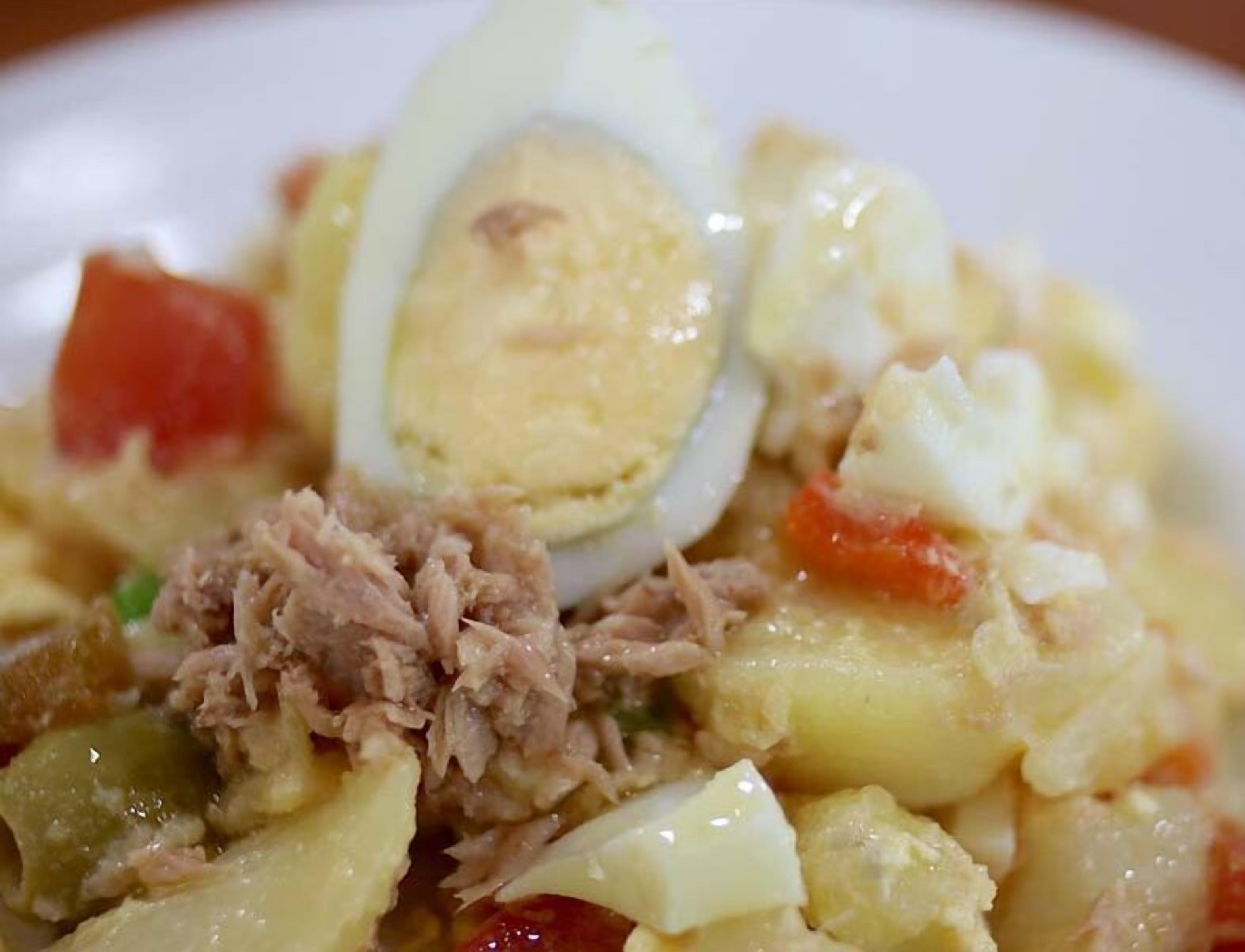 Une vue rapprochée d’un plat contenant des œufs durs en tranches, de la viande effilochée et des légumes coupés en dés.