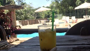 Een glas met een ijskoud drankje en een rietje op een houten tafel, in de buurt van een zwembad met ligbedden en parasols.
