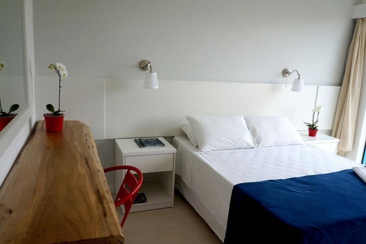 Ein Hotelzimmer mit Bett, Nachttischen, Schreibtisch, Stuhl und zwei Zimmerpflanzen.