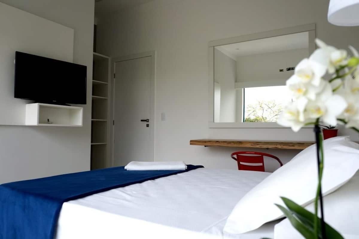 Ein modernes Hotelzimmer mit Bett, Flachbildfernseher, Spiegel und Fenster mit Blick.