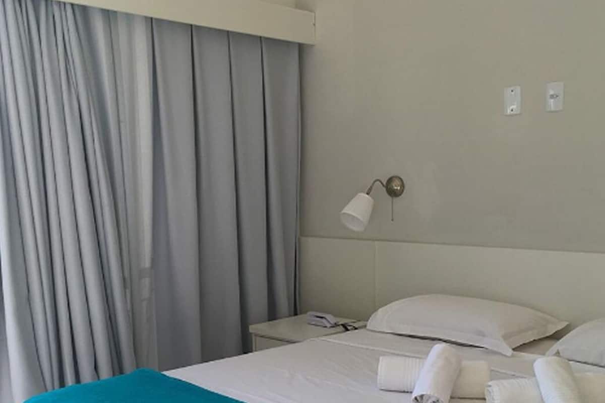 Ein Hotelzimmer mit Bett, Nachttisch, Lampe und Vorhang.