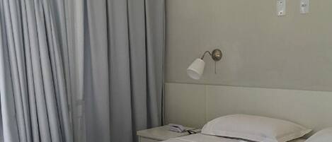 A hotel room with a bed, a nightstand, a lamp, and a curtain.