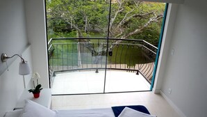 A bedroom with a large window overlooking a balcony with a view of trees and a body of water. - Flor Inn Praia Hotel (Florianópolis)