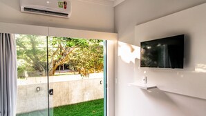 A modern hotel room with a large sliding glass door leading to a grassy outdoor area, a mounted flat-screen TV, and a ceiling air conditioning unit. - Flor Inn Praia Hotel (Florianópolis)