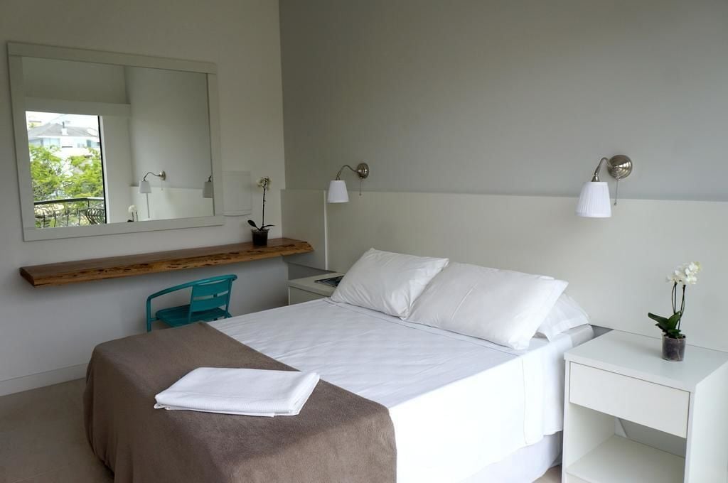 A modern hotel room with a large bed, a wooden shelf, a desk, and a mirror.