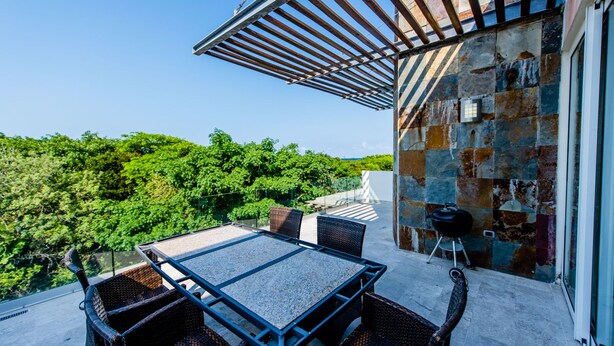 An outdoor patio with a table and chairs, a grill, and a stone wall.
