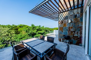 An outdoor patio with a table and chairs, a grill, and a stone wall. - Mamitas Village PH301 by PRP (Playa del Carmen)