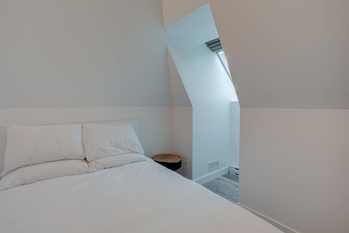 Une chambre à coucher moderne avec un lit, un petit tabouret en bois et un plafond en pente.