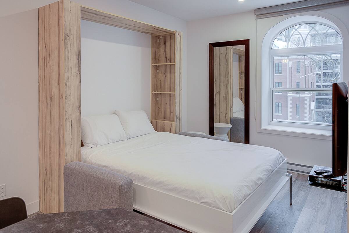 Une chambre moderne dotée d’une armoire intégrée, d’une grande fenêtre et d’une petite table.