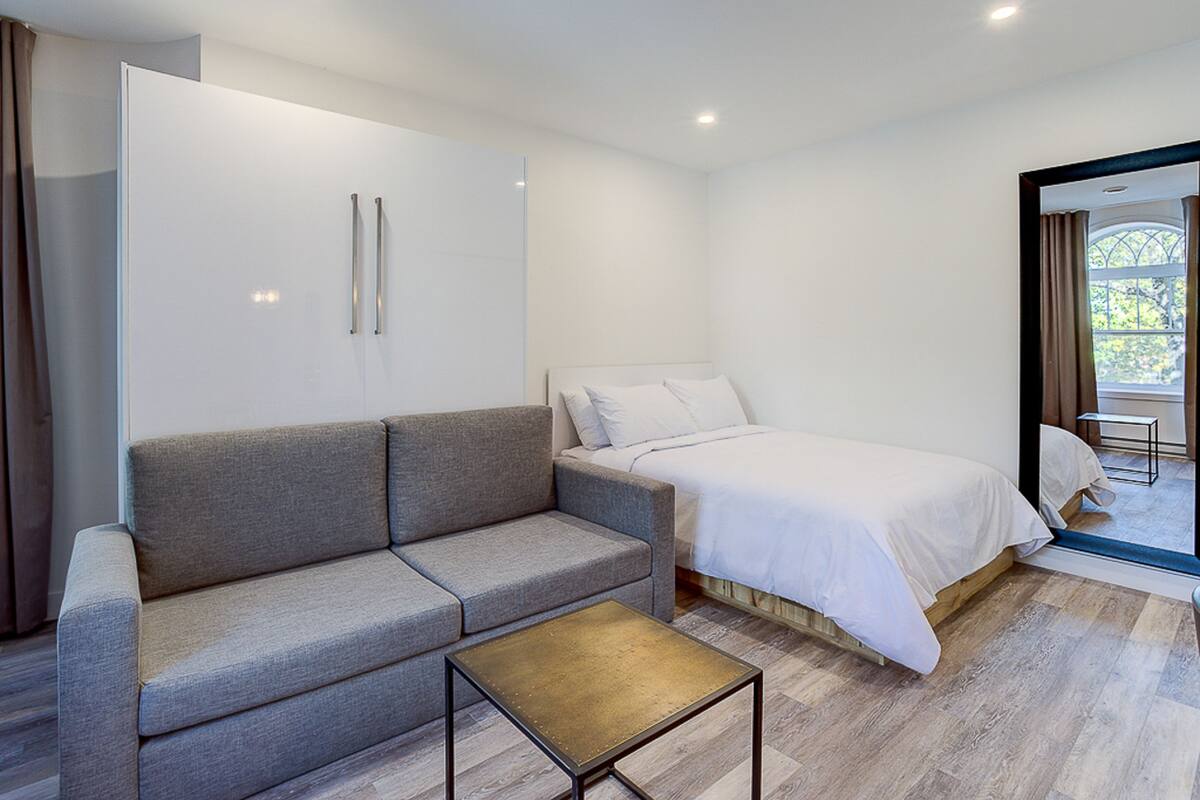Une chambre moderne avec un canapé gris, un lit simple et une petite table.