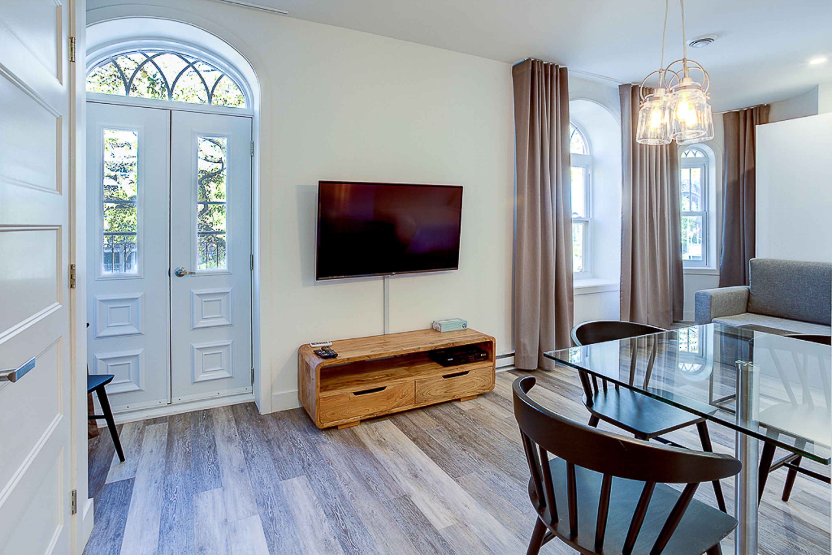 Un comedor moderno con una mesa y sillas de vidrio, un mueble bajo para la televisión de madera y un ventanal con cortinas.