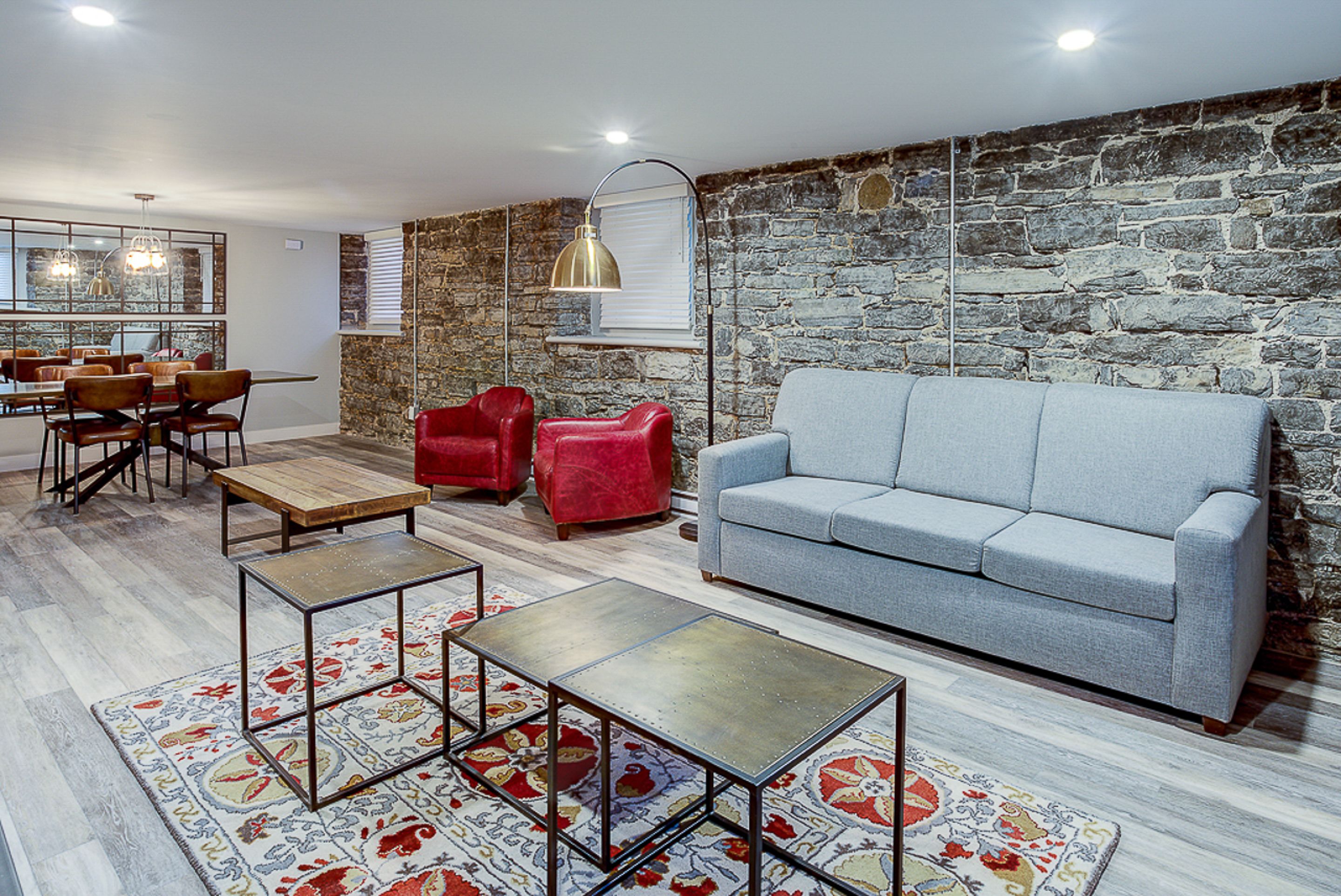 Una sala moderna con pared de piedra, un sofá gris, sillas rojas y una zona de comedor con muebles de madera.