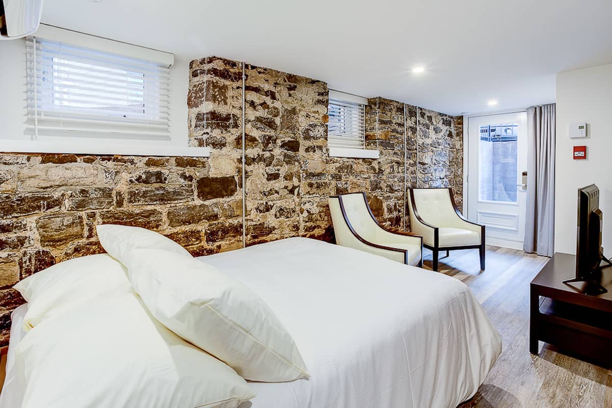 Une chambre avec un grand lit, un mur en pierre, deux chaises et un téléviseur.