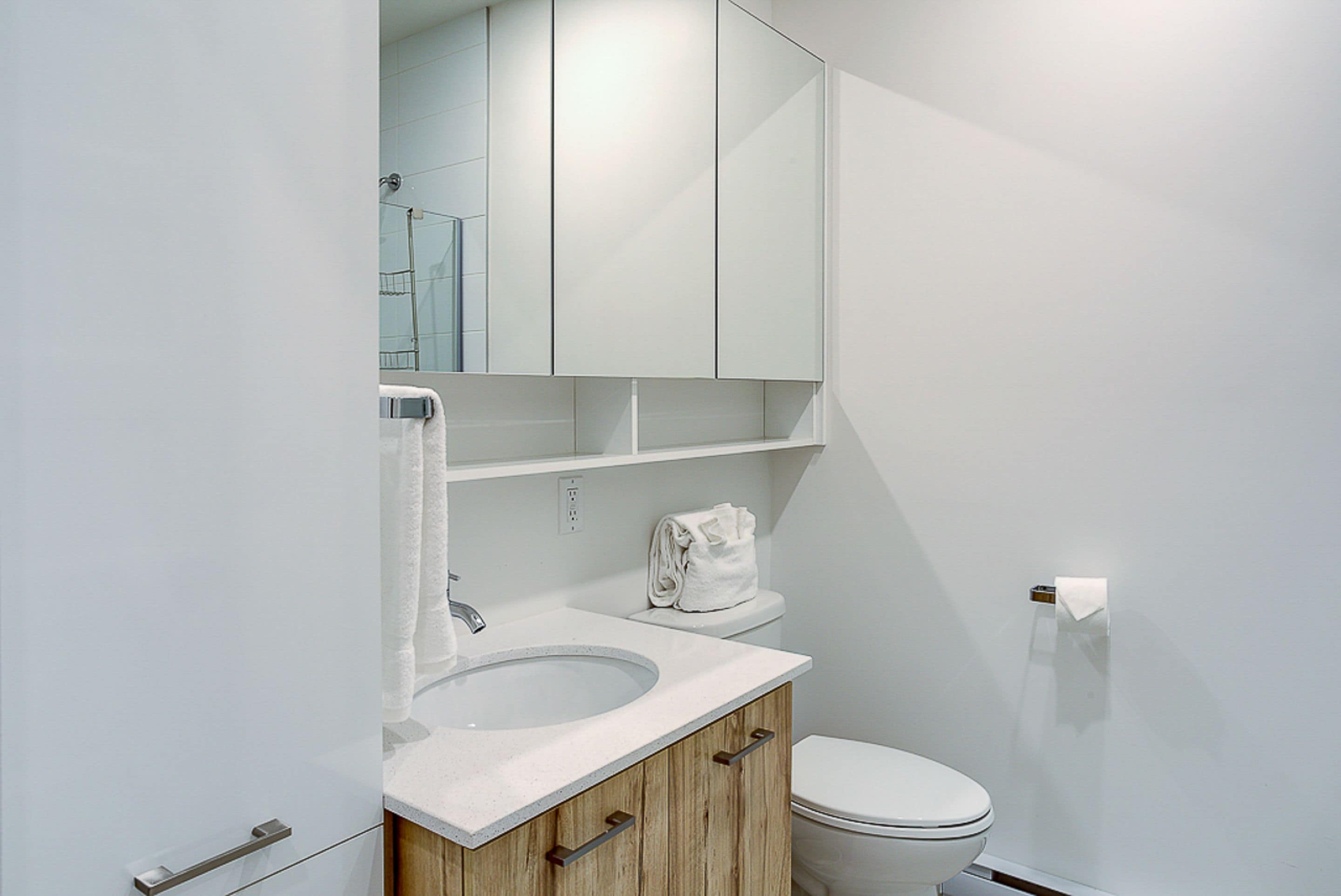 A modern bathroom with a white sink, wooden cabinet, and a toilet.