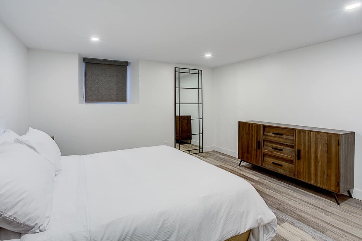 Une chambre avec un grand lit, une armoire en bois, une petite fenêtre avec un store et un miroir au mur.