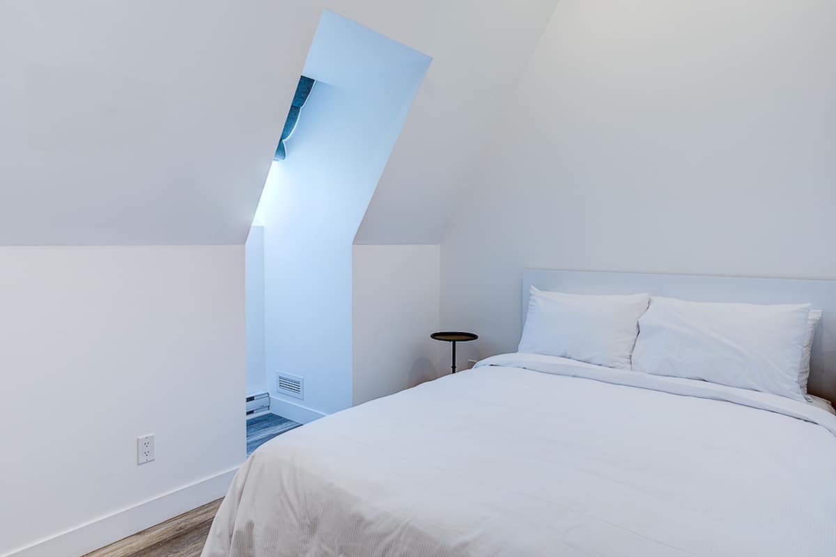 Une chambre moderne avec un plafond en pente, un lit recouvert de linge de lit blanc et une petite table de chevet.