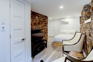 Un dormitorio con pared de piedra, una cama, una silla y un televisor.
