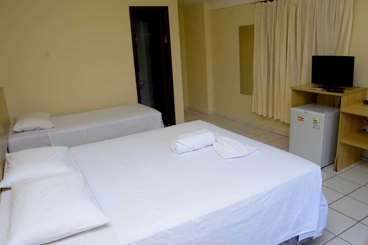 A hotel room with two single beds, a television, a small refrigerator, and a bathroom door.