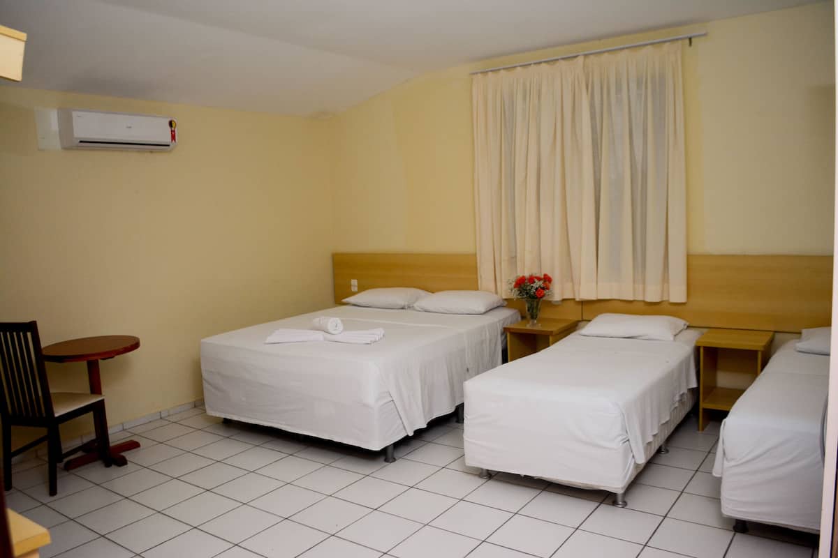 A hotel room with two single beds, a small table, a chair, and a window with curtains.
