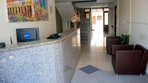 A reception area with a granite counter, a digital screen, a staircase, and a seating area with brown chairs. - Hotel Sambaquis (São Luís)