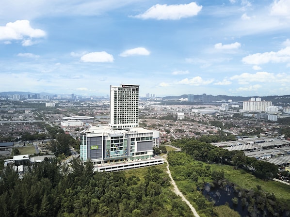 Un hotel moderno con una torre destacada, rodeado de vegetación y un paisaje urbano al fondo.