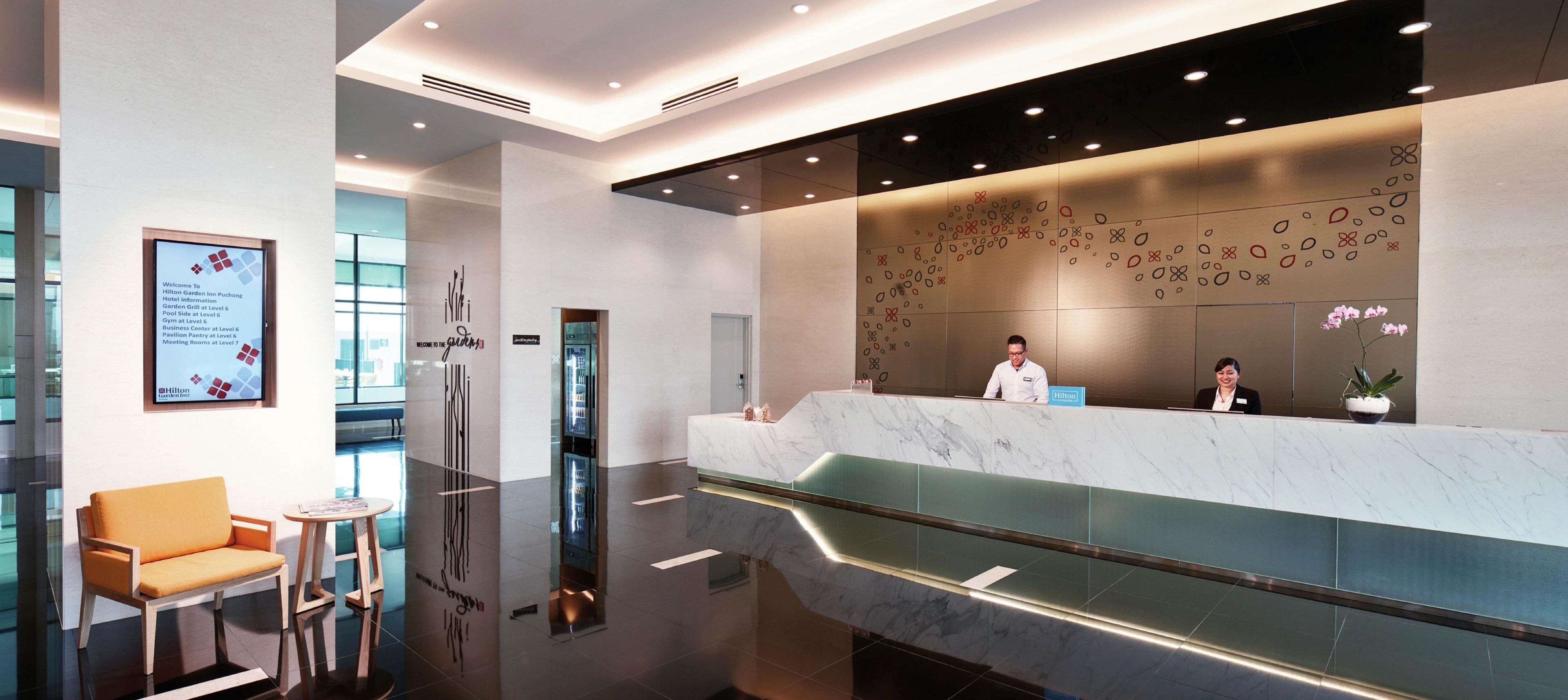 Un moderno hall de hotel con mostrador de mármol, un ascensor de vidrio y un área de estar con sofá y mesa.