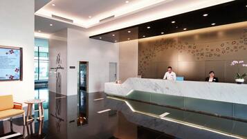 Un moderno hall de hotel con mostrador de mármol, un ascensor de vidrio y un área de estar con sofá y mesa.
