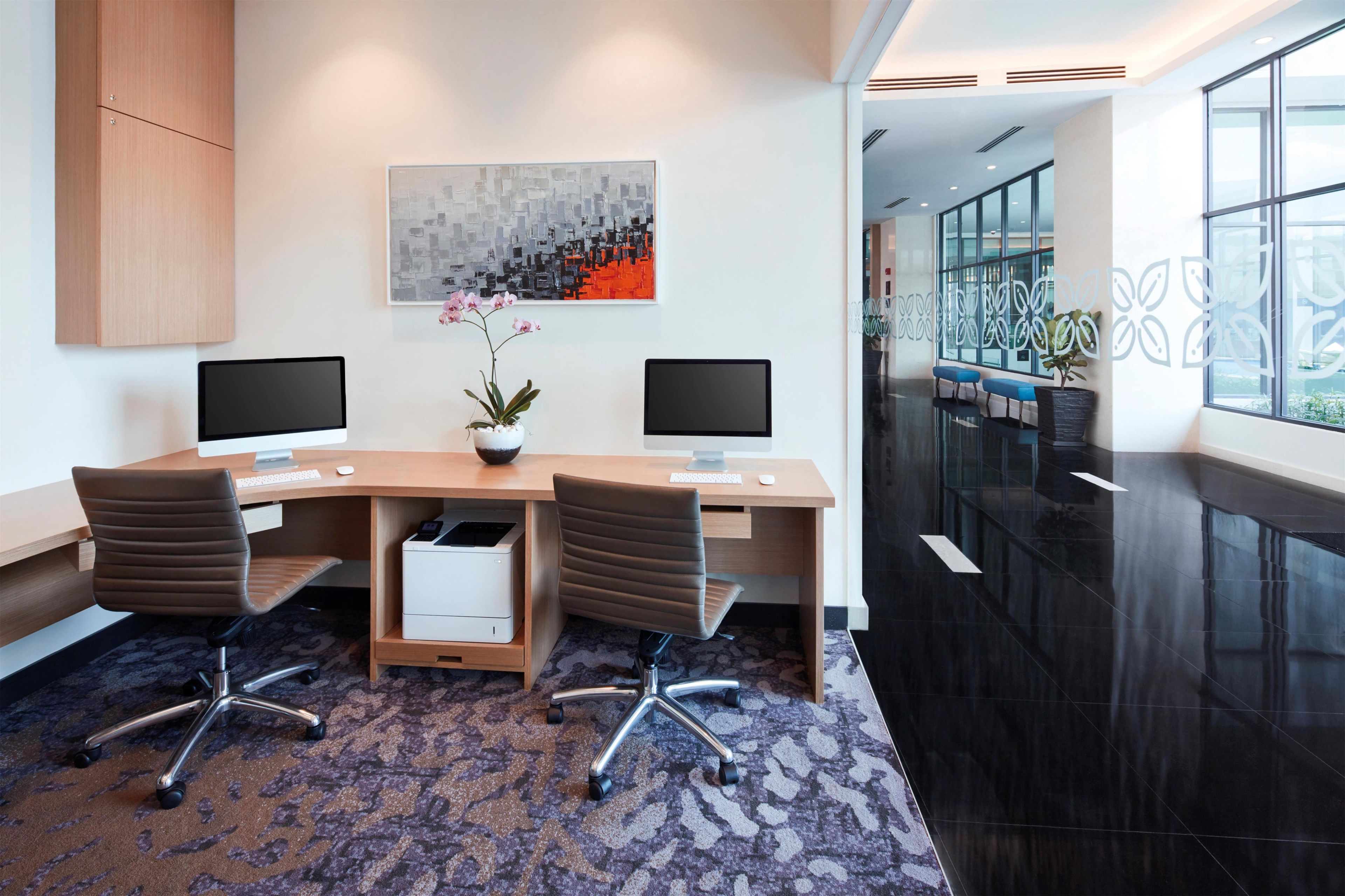 A modern office space with two desks, chairs, a potted plant, and a large abstract painting on the wall.