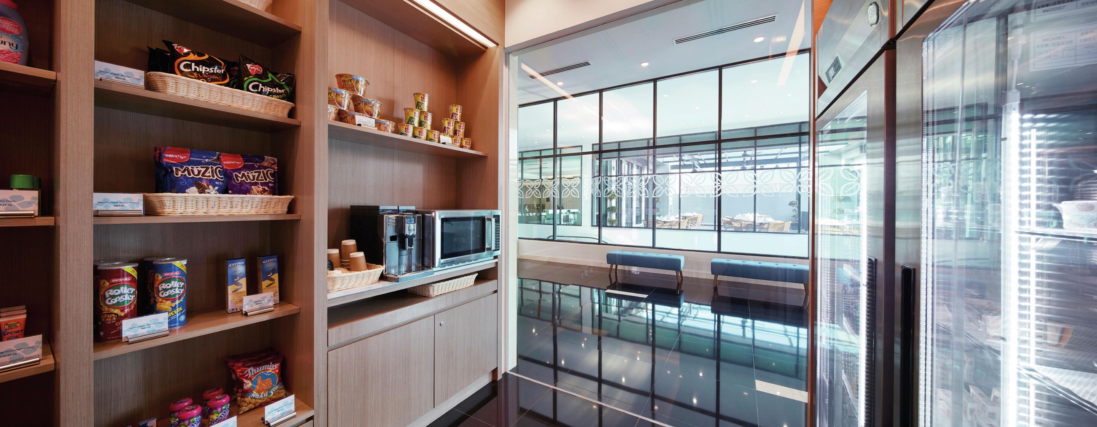A modern interior with shelves stocked with snacks, a coffee machine, and seating with a view.