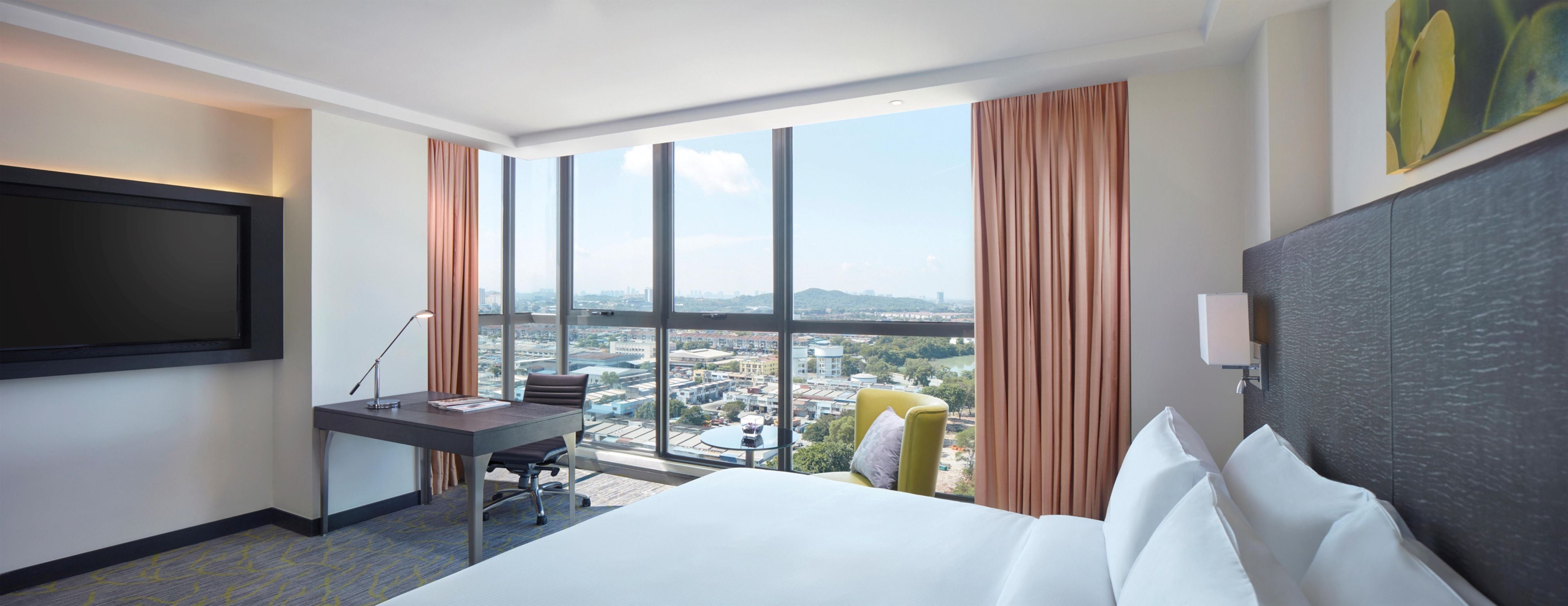 Habitación de hotel con cama, escritorio, silla y un ventanal con vistas a la ciudad.