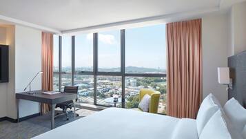 Habitación de hotel con cama, escritorio, silla y un ventanal con vistas a la ciudad.