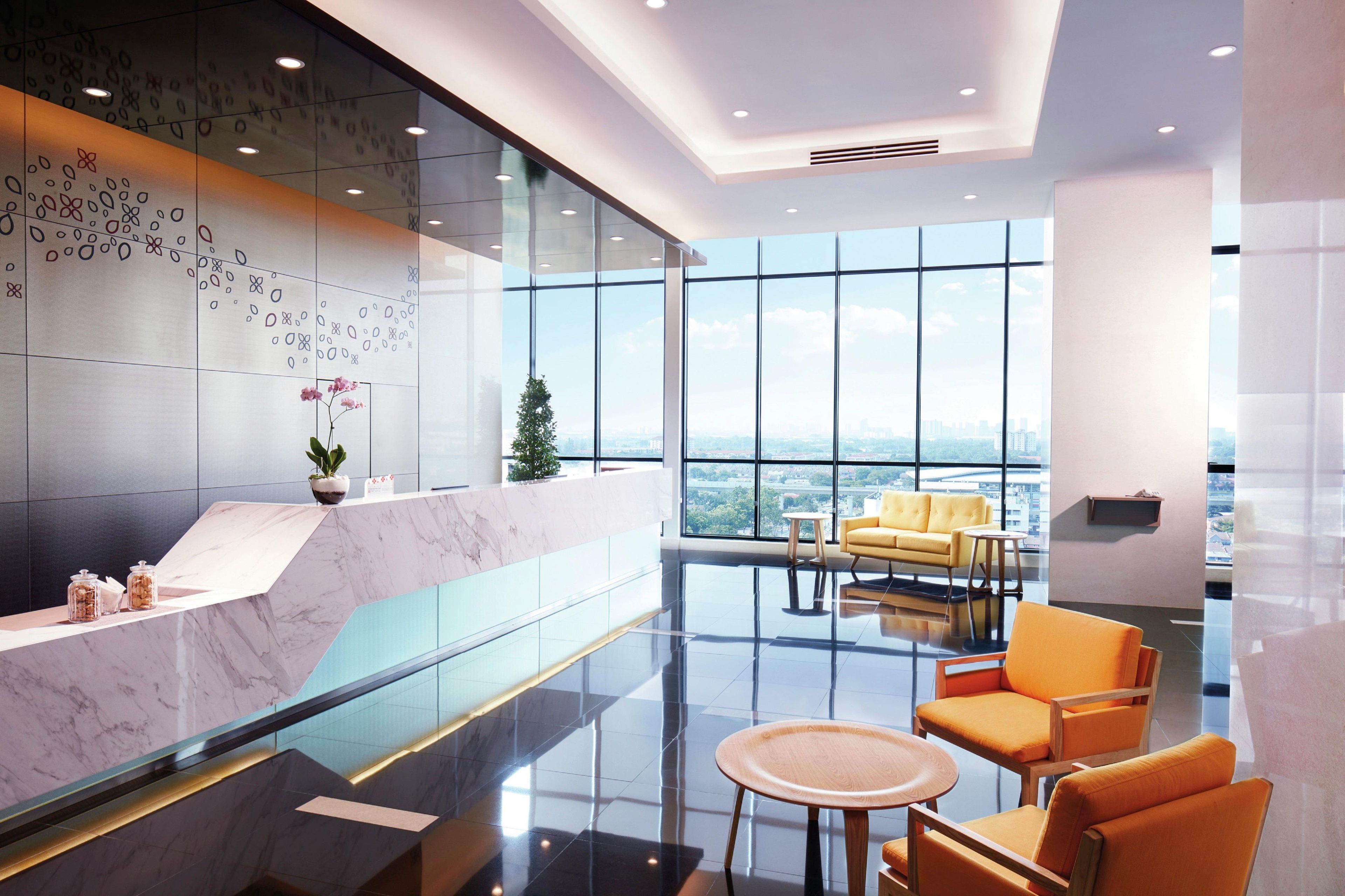Un hall d’entrée moderne avec un comptoir de réception en marbre, un mur en verre, une vue sur la ville et un espace détente agrémenté de fauteuils orange.