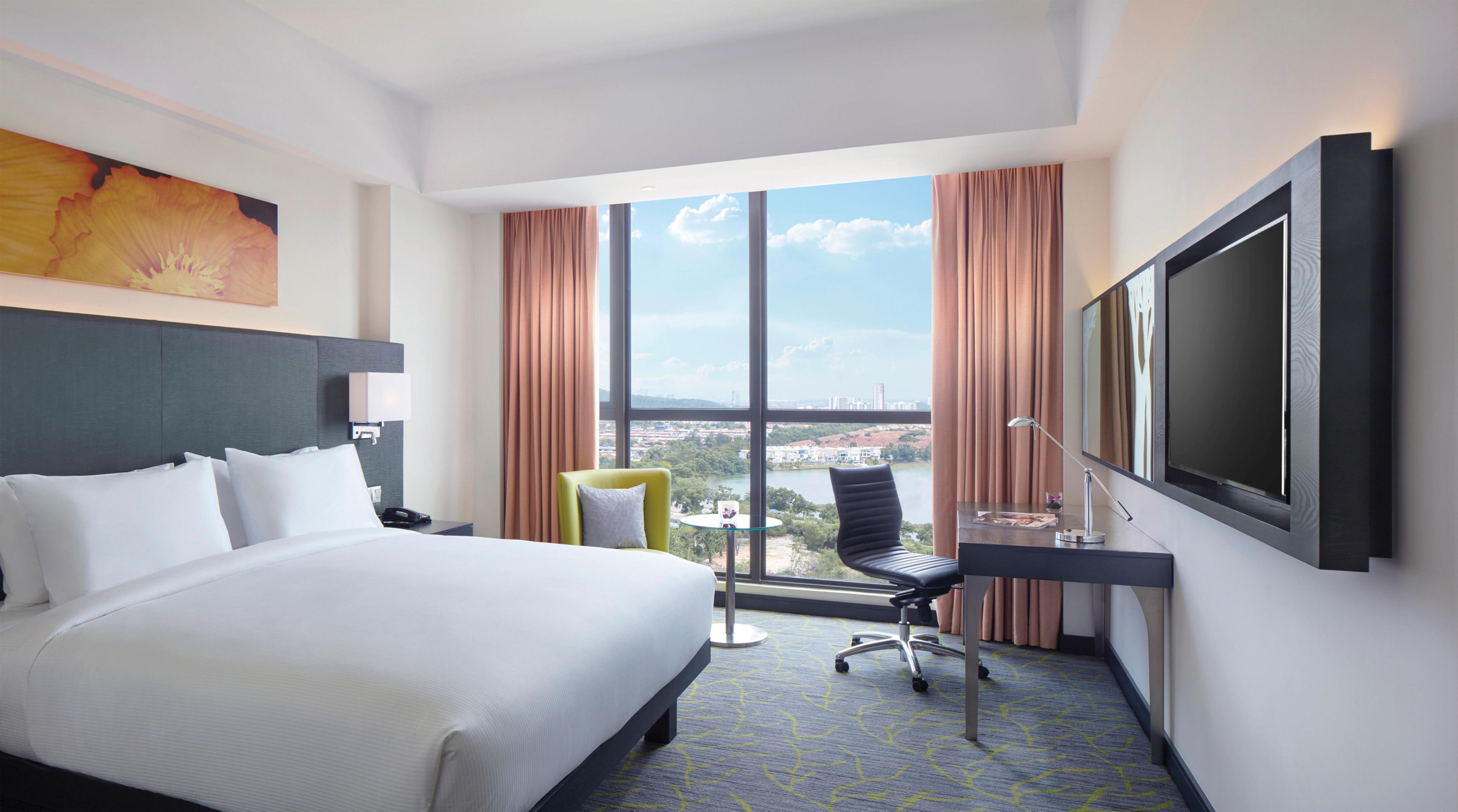 A hotel room with a large bed, a desk, a chair, and a TV.