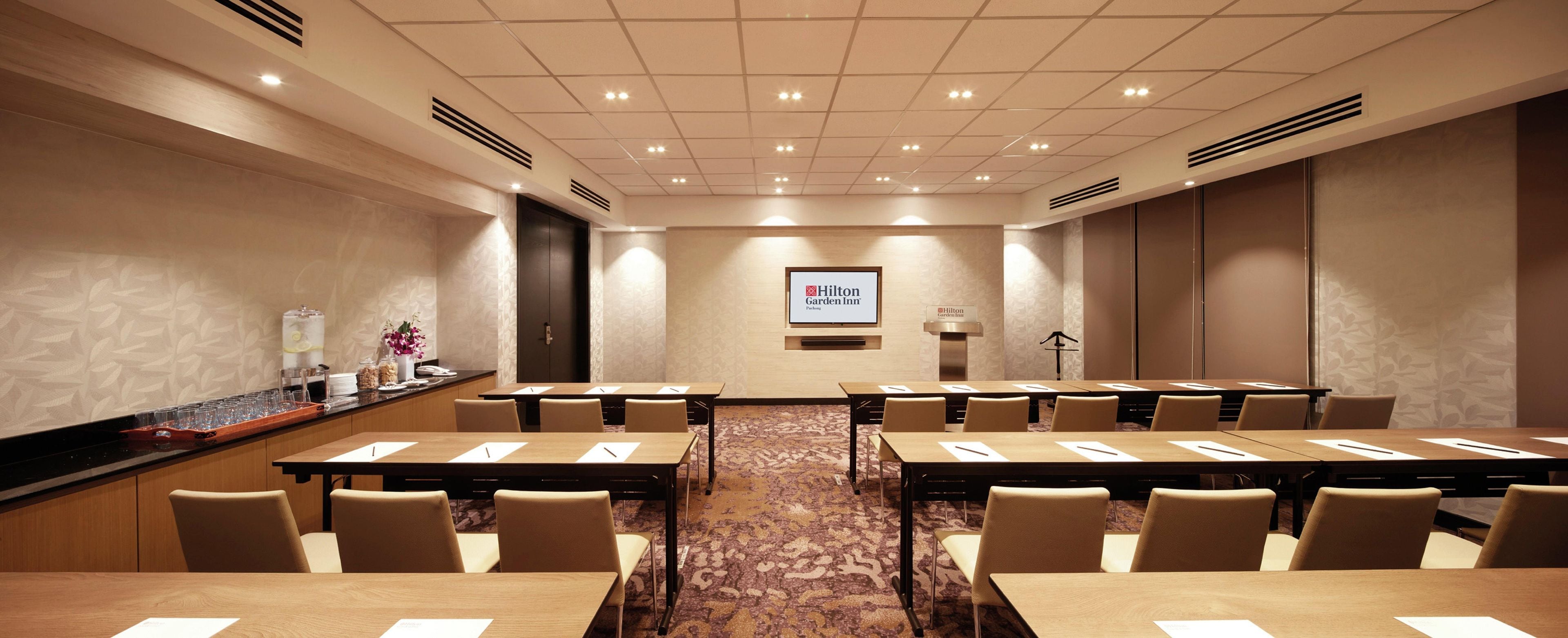 A conference room with multiple tables and chairs, a podium, and a screen displaying the Hilton Garden Inn logo.