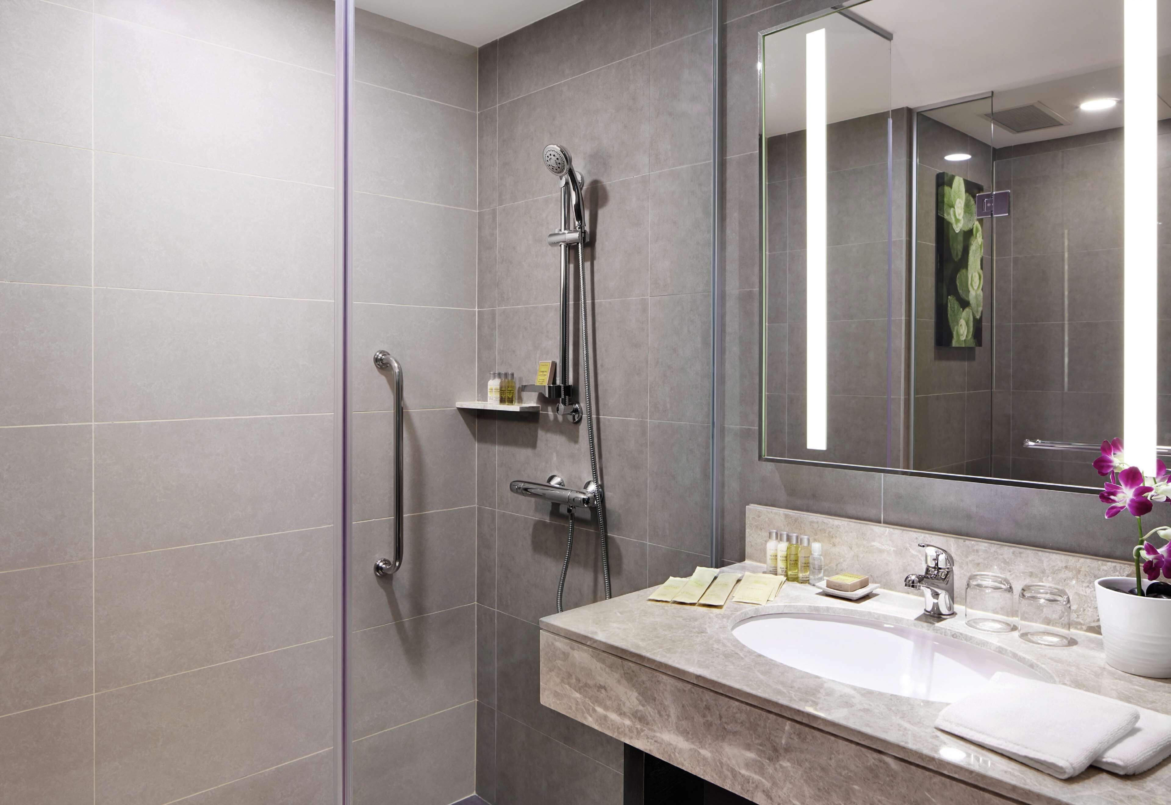 A modern bathroom with a walk-in shower, a large mirror, and a marble sink.